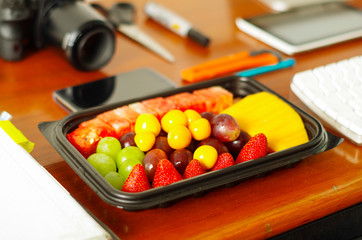 Close up of a healthy breakfast, fruit salad packed in plastic box on wooden table