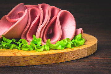 Sliced sausage with salad on a round wooden board. © detry26