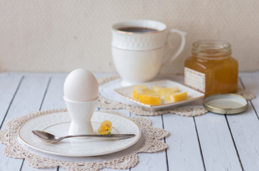 Beautiful Breakfast. Boiled egg white on a white stand for the eggs on a white plate on lace crochet doily. Tea in a white Cup, slices of lemon on a saucer, homemade lemon jam. Natural lighting.