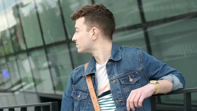 Handsome man looks stylish while standing next to the modern building, steadycam shot
