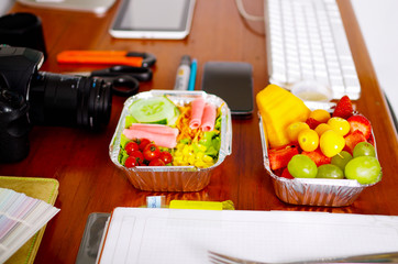 Delicious mediterranean-Style fresh salad with ham and fruit salad on aluminium box surrounded of office stuffs, break time in office