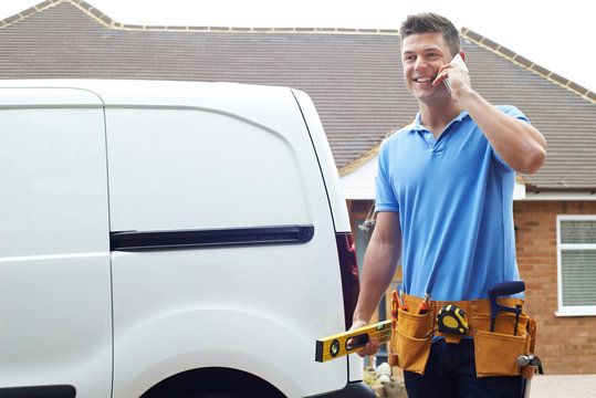 Builder With Van Talking On Mobile Phone Outside House