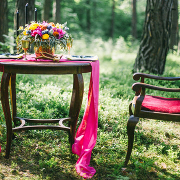 decorated wooden table served for two in the garden on grass on the riverbank. Boho and rustic style decoration with flowers, peacock feather, candles, clayware. Romantic date, table setting