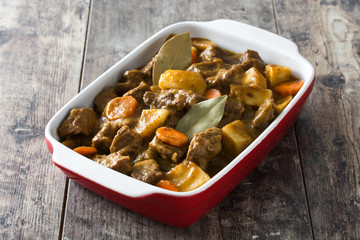 Beef meat stewed with potatoes, carrots and spices in ceramic pot on wooden table
