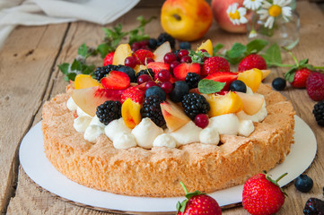 Homemade dacquoise cake with wipped cream cheese garnished with summer berries and peaches, close up.