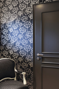 Resting corner with gray door with black wallpaper and golden flowers and gray armchair