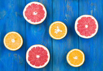 Fresh half cut grapefruit and orange on a blue wooden background, close up view.