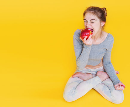 Beautiful young yogini woman sitting down in lotus pose and eating apple, healthy food concept