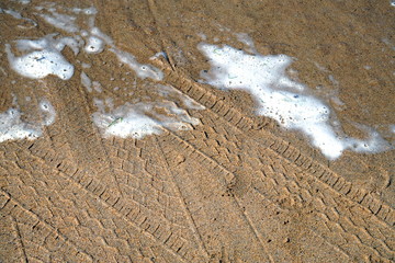 Fototapeta na wymiar Tyre or tire tracks on a sandy beach being washed by white surf
