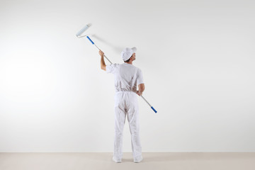 Rear view of painter man looking at blank wall, with paint roller stick, isolated on white room