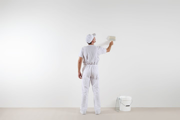 Rear view of painter man looking at blank wall, with paint brush and bucket, isolated on white room