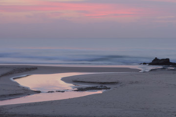 A placid early morning at Baggies Beach near Durban, South Africa. Dawn at the beach, showing a stream from the lagoon, flowing down to the surf-line.