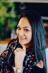 Naklejka premium Portrait of young dreaming girl in cafe. Beautiful girl sits in coffee shop and looks,Girl smiling, hand near face