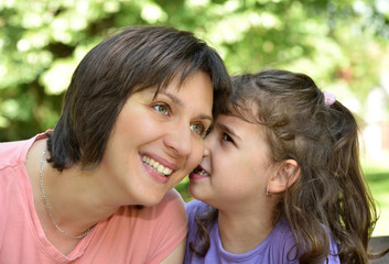 Daughter whispering secret into ears of smiling mother