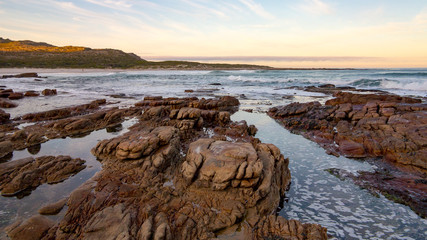 Fototapeta na wymiar Early morning tide and surf at Scarborough on the Cape Peninsula in South Africa. This photograph is a wide-angle shot of the rocks and surf on a calm morning.