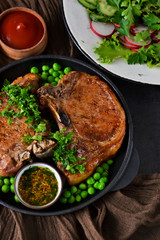 Steak grilled with a garnish of green peas and tomato sauce in a cast-iron frying pan