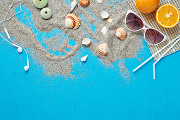 Summer set. Beach vacation accessories sunglasses and oranges flat lay on sand with seashells. Isolated on blue background.