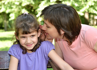 Mother whispering secret into ears of smiling daughter