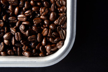 Roasted coffee beans in a metal tray on black background