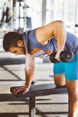 Fototapeta na wymiar Young handsome man working out with dumbbells in a fitness gym