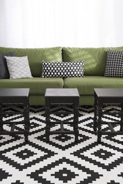 Salon avec canap&eacute; vert, coussins et tapis design noir & blanc et tabourets noirs