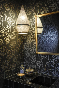 Black bathroom with black and gold floral wallpaper, Moroccan lamp with subdued light and black tiles