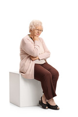 Sad mature woman sitting on a cube