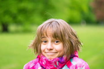 Emotional portrait of attractive caucasian little student girl with beautiful brown eyes in spring city park. Funny cute smiling child looking at camera - close-up, outdoors.