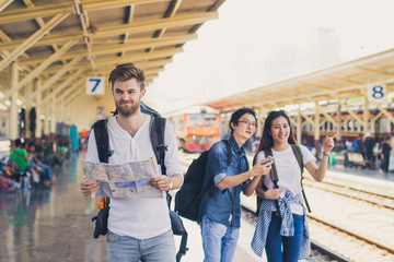 Multi ethnic diverse group of friends traveling together while using mobile phones and map in transportation hub. Backpacker, travel or holiday concept.