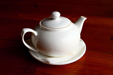 White teapot and the saucer on the wooden table alone