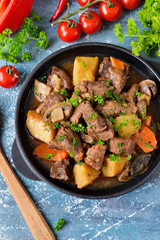 Meat goulash with vegetables, potatoes and mushrooms on concrete, grunge background