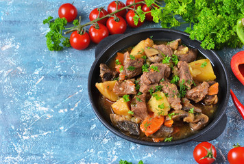 Meat goulash with vegetables, potatoes and mushrooms on concrete, grunge background
