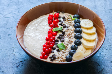 Super food smoothie bowl with oats, cootage cheese, milk, berries, sunflower seeds and banana on a black slate background.