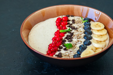 Super food smoothie bowl with oats, cootage cheese, milk, berries, sunflower seeds and banana on a black slate background.