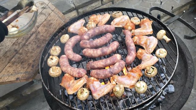 Mixed Grill BBQ - Man arranging sausages, chicken wings and mushrooms on a barbecue