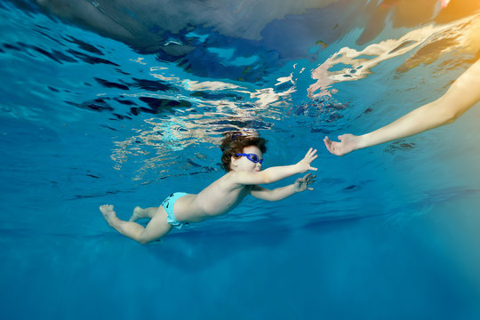 Little girl swims underwater in the pool and reaches for the hand of the mother. Portrait. Bottom view from under the water. The landscape orientation