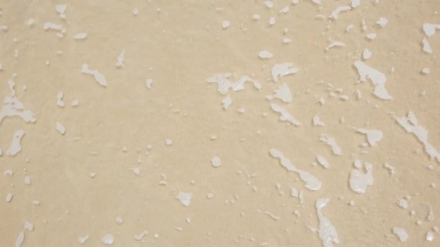 Top-down view of "SEA" written in the sand, partially washed away by a gentle wave, capturing a transient moment at the beach