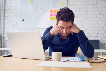 Depressed young man looking on financial documents working at office