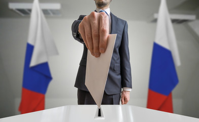 Election or referendum in Russia. Voter holds envelope in hand above ballot. Russian flags in...
