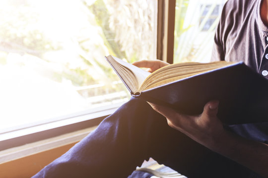 young man is sitting reading in the window in the room with soft-focus in the background. over light and vintage colors tone