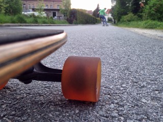Longboard im Vordergrund und Longboarder im Hintergrund auf Straße