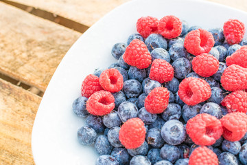 Himbeeren und Blaubeeren auf einem weißen Teller vor Holz Hintergrund