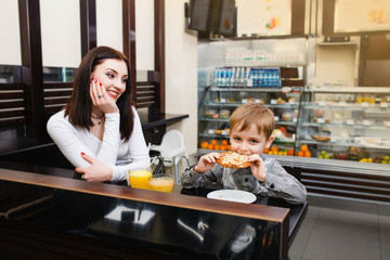 Mom with a small son is sitting in a cafe, drinking juice and eating sweets
