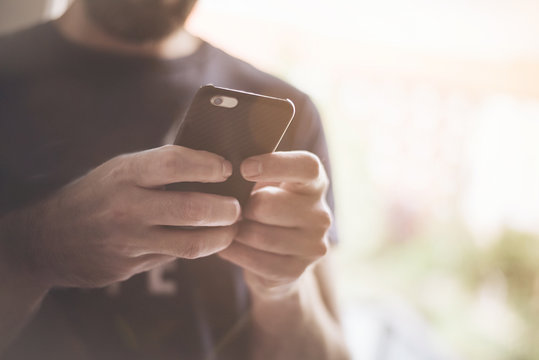 young man standing in sunlight texting on smartphone