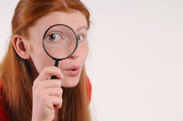 Portrait of a young red hair teen woman looking at the camera through a magnifying glass