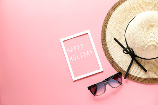 woman hat and happy holiday text in White picture frame and sunglasses on pink background ,copy space,flat lay