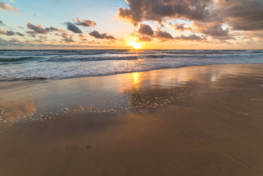 Ocean sandy shore with soft waves against sunrise sky on the background