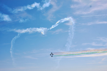 A figure in the sky in the shape of a heart from a smoke and ahead of an air fighter against a blue sky. Bright air show