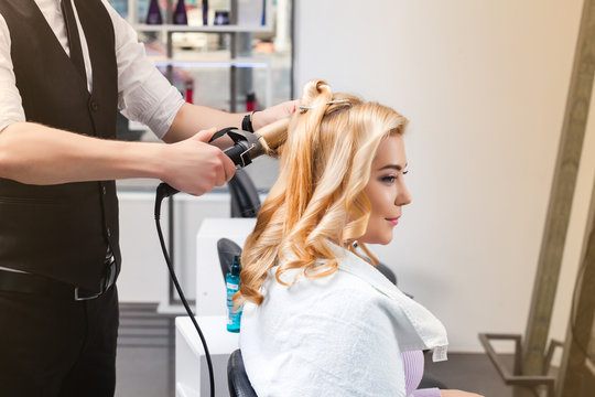 handsome Hairdresser does a hairstyle for a blonde girl in a beauty salon