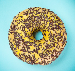 Glazed donut with colorful sprinkles on blue pastel background.